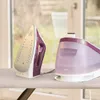 A steam iron and its base unit are placed on an ironing board in front of a window. Produktbild-Vorschau