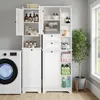 A white storage cabinet with multiple shelves and drawers, a laundry basket, and a washing machine next to it, in a room with a window and a plant. Anteprima dell’immagine prodotto