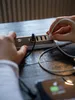 Hands plugging a USB cable into a multi-port USB charging station on a wooden table, with a smartphone also visible and charging. Náhľad obrázku produktu