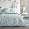 A neatly made bed with a floral pattern duvet cover and pillows, set against a white wall with decorative branches in vases and a white chair with a green lantern. Produktbild-Vorschau