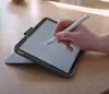 A hand holding a stylus is writing on a tablet, which is placed on a wooden table. Náhled obrázku produktu