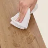 A hand is wiping water off a wooden surface with a white cloth. Náhled obrázku produktu