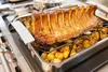 A roasted rack of pork with potatoes in a roasting pan on a stovetop. Produktbild-Vorschau