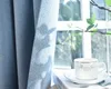 A close-up of a blue curtain with sunlight filtering through, casting shadows. A white coffee cup and saucer are on a book in the foreground. Produktbild-Vorschau