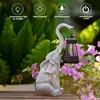 An elephant statue holding a lantern in a garden setting. Produktbild-Vorschau