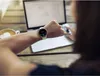 A person is using a smartwatch while working on a laptop at a wooden table, with a cup of coffee nearby. Voir les images du produit