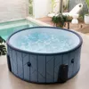 An inflatable hot tub filled with bubbling water is placed on a patio next to a swimming pool. The background shows a wooden deck with lounge chairs and plants. Náhled obrázku produktu