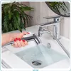 A hand with red nail polish is holding a bidet spray head, spraying water into a white sink. A modern faucet is visible behind it, and a lush green plant is in the background. Náhľad obrázku produktu
