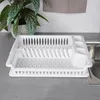 A white plastic dish rack is placed on a gray countertop next to a sink. Produktbild-Vorschau
