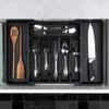 A top-down view of a black cutlery organizer filled with various utensils and a knife, placed inside a kitchen drawer. Produktbild-Vorschau