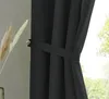 A close-up view of a black curtain tied back with a fabric band, with a hint of greenery visible through the window. Produktbild-Vorschau