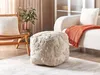 A modern living room with a beige pouf, a chair with a cushion, and a sofa with an orange throw. Produktbild-Vorschau
