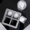 A grey ice cube tray with four large square ice cubes, one of which is outside the tray next to a glass with an ice cube inside, on a black reflective surface. Podgląd zdjęcia produktu