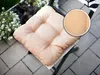 A close-up of a beige seat cushion on a chair, with a planter of white flowers in the background. Produktbild-Vorschau
