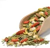 A wooden scoop filled with a mixture of dried mate tea leaves, goji berries, and other dried fruits, spilling onto a white surface. Voir les images du produit