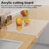 A clear acrylic cutting board is placed on a wooden countertop, with oranges and a bowl of fruit in the background. Produktbild-Vorschau