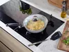 A frying pan with food cooking inside is placed on a modern induction stovetop, with kitchen utensils and ingredients nearby. Produktbild-Vorschau