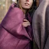 Two people wrapped in blankets in a forest setting. Produktbild-Vorschau
