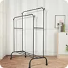 A double-tiered metal garment rack with a shoe shelf at the bottom, set against a white wall with subtle paneling. A small cabinet with two drawers and a framed picture are visible to the right. Anteprima dell’immagine prodotto