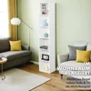 A tall, narrow white bookshelf is placed in a living room setting next to a sofa and armchair. The bookshelf is filled with decorative items and books. The room has light green walls and wooden flooring. Produktbild-Vorschau