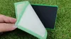 A hand is holding a green and white cleaning pad over a green grassy surface. Another black and green pad is visible in the background. Produktbild-Vorschau