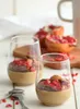 Two glasses of dessert topped with pomegranate seeds and almonds, with a halved pomegranate in the background. Produktbild-Vorschau