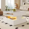 A modern living room with a white coffee table featuring glass and acrylic elements, illuminated by LED lights. The table is placed on a patterned rug in front of a sofa and a large window with plants. Produktbild-Vorschau