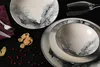 A set of porcelain dishes with a marbled gray and white pattern, arranged on a black surface. Anteprima dell’immagine prodotto