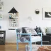 A cozy living room scene featuring a blue armchair with a blanket and pillows, a black leather sofa, and a wall-mounted advent calendar. Podgląd zdjęcia produktu