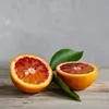 Two halves of a blood orange and two green leaves are placed on a wooden surface against a gray background. Anteprima dell’immagine prodotto