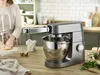 A kitchen scene with a stand mixer and pasta attachment, and a person preparing dough. Produktbild-Vorschau