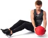 A man is sitting on the floor with his legs extended, holding a red slam ball. Produktbild-Vorschau