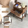 A bedside table with a drawer and shelf, placed next to a bed. The table has a phone, coffee cup, and flowers on top. Podgląd zdjęcia produktu