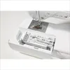 A close-up view of the sewing machine's accessory storage drawer, showing various presser feet and other sewing tools. Produktbild-Vorschau