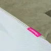 A close-up view of a tan fabric product with a white mesh side, featuring a pink tag with text. Podgląd zdjęcia produktu