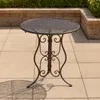 A round metal garden table with an ornate base is shown on a paved patio. Produktbild-Vorschau