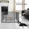 Two dogs are in a living room setting with a fireplace and a sofa. One dog is inside a playpen, and the other is lying on the floor. Náhled obrázku produktu