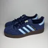 A pair of navy blue Adidas Handball Spezial sneakers with light blue stripes and a brown sole, displayed against a light gray background. Voir les images du produit