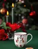 A Christmas-themed scene with a mug, candles, and a Christmas tree in the background. Voir les images du produit