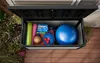 An open storage box filled with various fitness equipment, placed on a wooden deck next to some plants. Produktbild-Vorschau