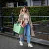 A woman walks down a brick path carrying a large green tote bag with flowers inside. Náhled obrázku produktu