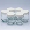 Six small glass jars with white lids arranged in a semi-circle against a light gray background. Produktbild-Vorschau