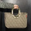 A person's arm and hand holding a quilted tote bag with a metal frame. Náhľad obrázku produktu