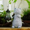 A garden statue of a cat holding a lantern, surrounded by plants. Produktbild-Vorschau