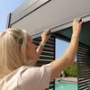A woman is adjusting the louvers of a modern pergola on a sunny day, with a swimming pool and greenery in the background. Produktbild-Vorschau
