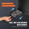 A hand is shown pulling out an ash drawer from a black outdoor fire pit. The ash drawer is filled with ashes. Produktbild-Vorschau