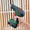 A hand holding a cordless drill in front of a wooden background. Náhled obrázku produktu