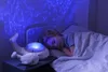 A child sleeping in bed with a whale-shaped night light projecting blue light onto the wall. Anteprima dell’immagine prodotto