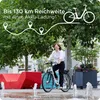 A woman riding an e-bike in a park-like setting with fountains and modern red seating. Anteprima dell’immagine prodotto
