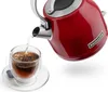 A red KitchenAid kettle pouring hot water into a glass teacup with a tea bag. Produktbild-Vorschau